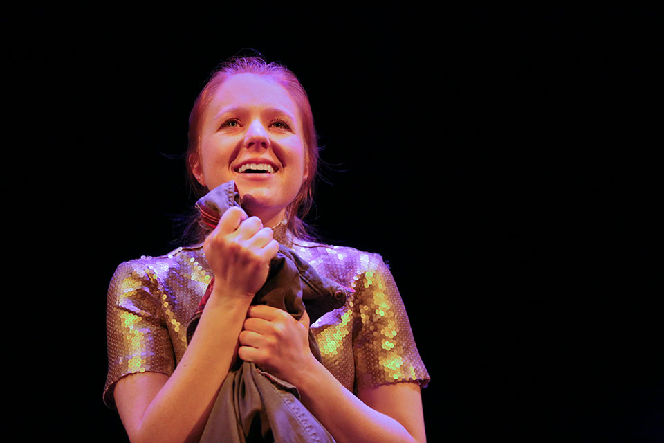 Actress performing on stage smiling and clutching a garment