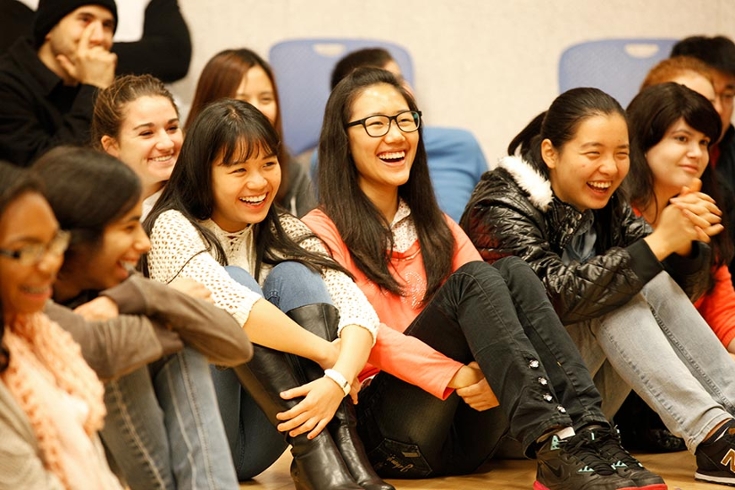 Group of theater students seated on the floor of a classroom smiling