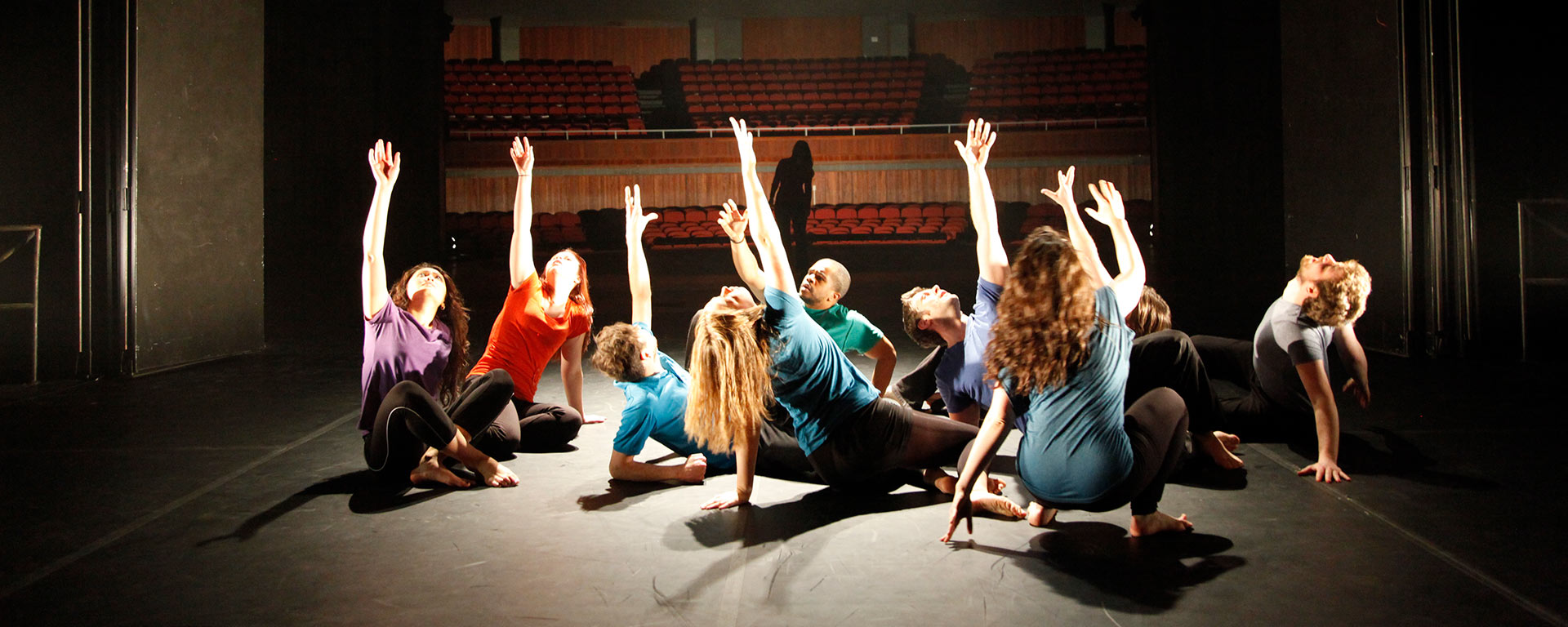 Group of students on stage crouched down toward the floor, reaching with one arm outstretched upward