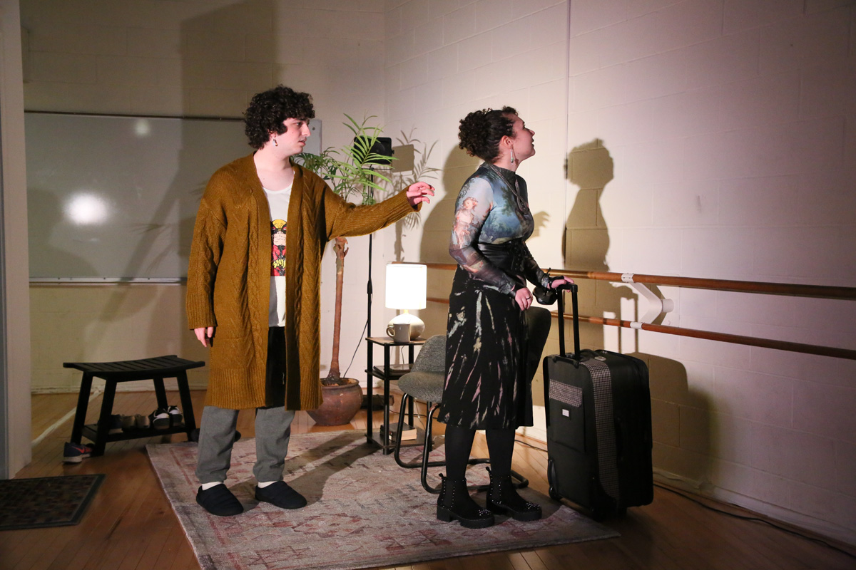 Two people looking toward a wall, one with a suitcase