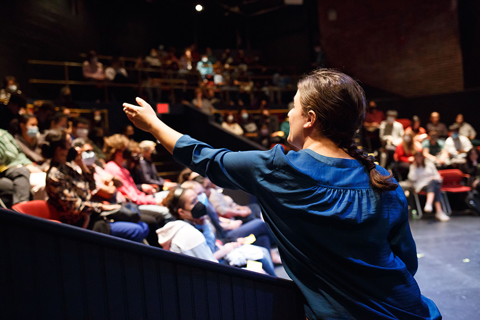 Actor looking toward the audience holding a microphone with arm outstretched