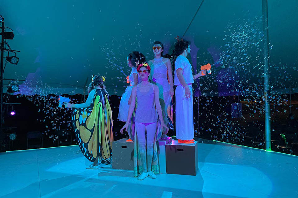 Actors performing in an outdoor tent with bubble machines