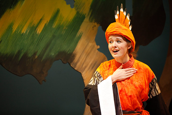 Female student dressed in orange costume and headpiece performing on stage in The Conference of the Birds