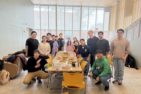 A group of students stand with Professor Xiwen Lu in front of a table full of Chinese food