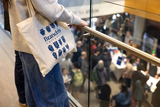 A student holding a Brandeis-labeled cloth bag looks over the Shapiro Campus Center from the second floor