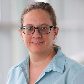 Kim wears glasses and has her blonde hair in a ponytail. She wears a blue button-up blouse.