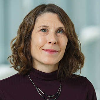 Margaret has wavy brown hair and wears a black blouse.