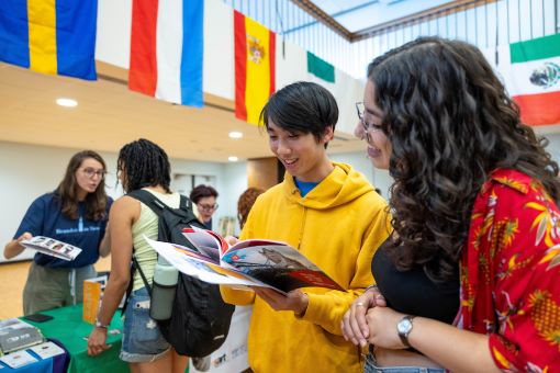 Two students look through a pamphlet at a study abroad fair