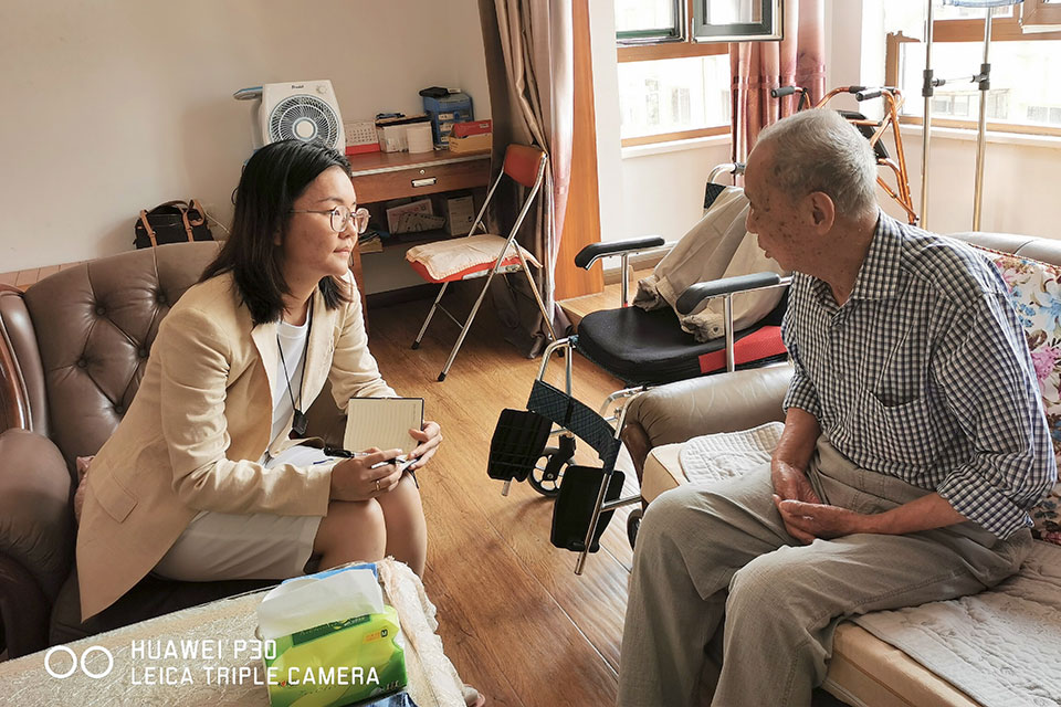 A student sits and talks with an elderly man in his home