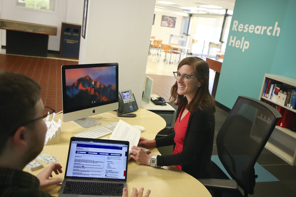 Staff at desk in library talking to student