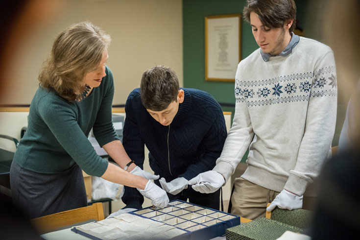 Librarian assisting two students as they look at archive materials