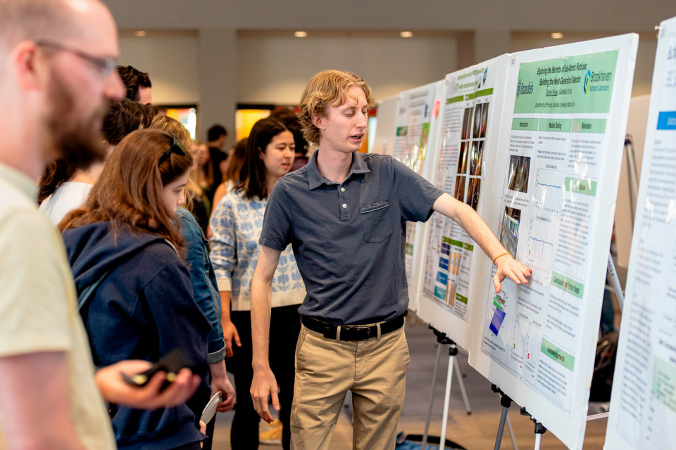 Daniel House stands in front of his poster, describing his research to his peers