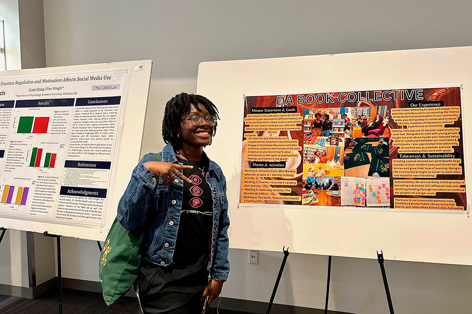 A young woman smiles and poses in front of two research posters at an academic symposium. 