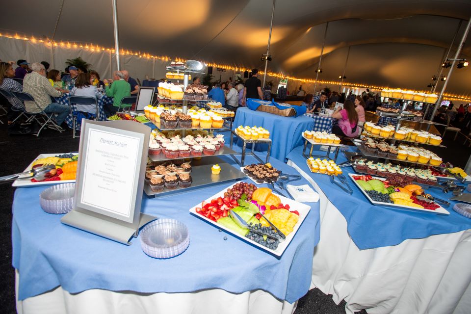 Tables with food are lined up beneath a tent
