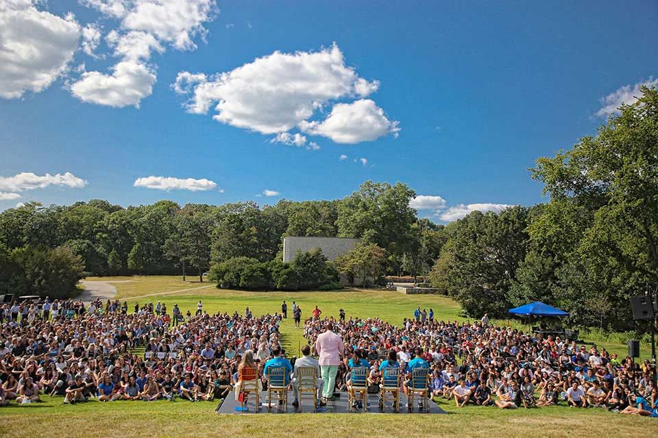 view from behind six people addressing a large group seated on the lawn