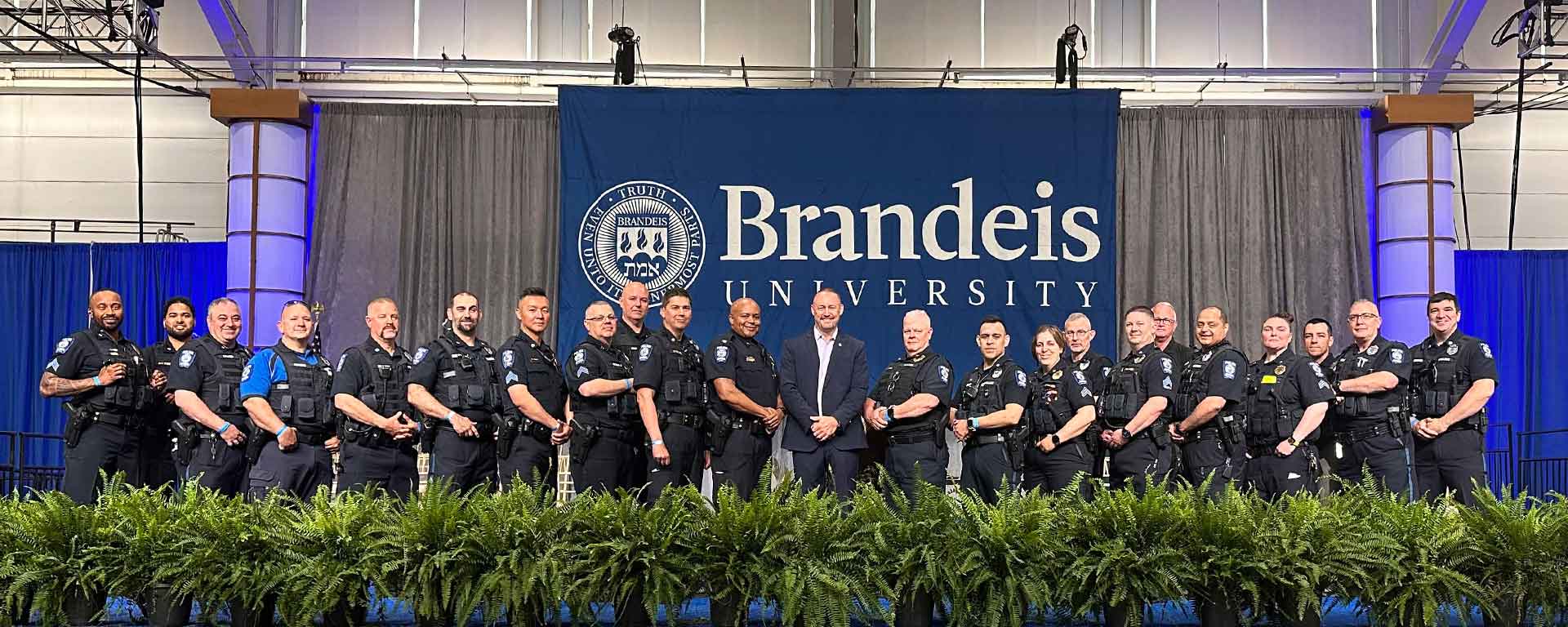 The Brandeis police in uniform stand in front of a large Brandeis logo