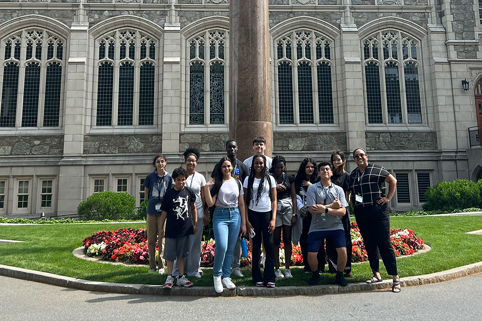 A group of students smile and stand in front of a building at Boston College.