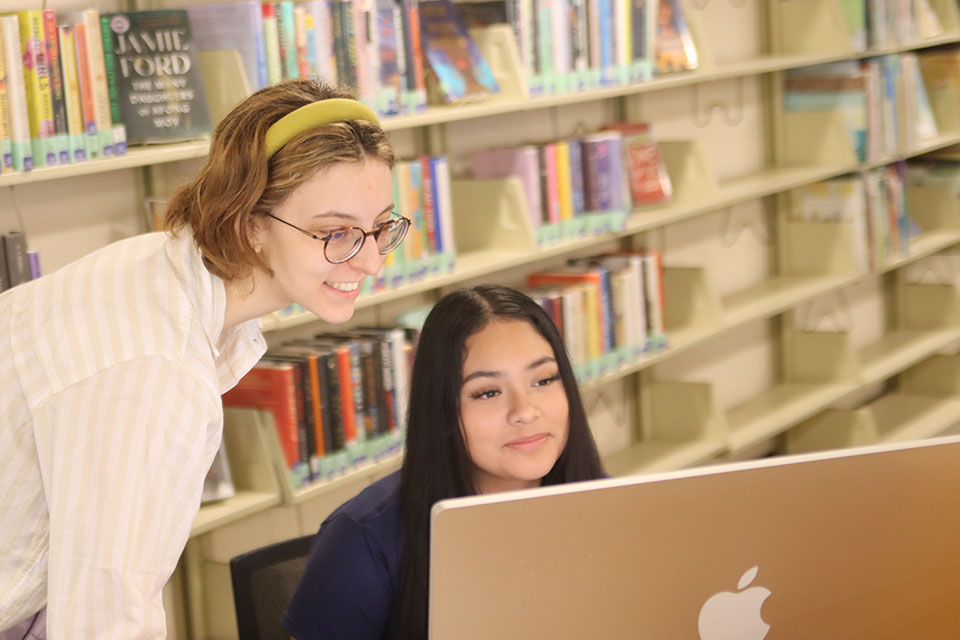 Two people look at a computer in a library.