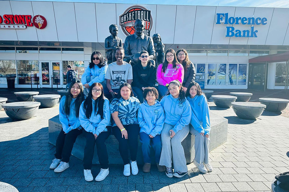 Students smile for a group photo in front of a statue.