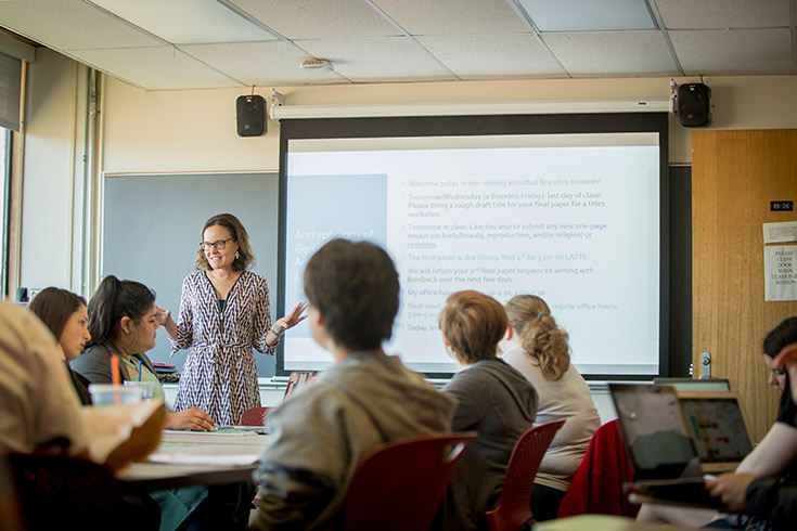 Professor Sarah Lamb instructing a class with a PowerPoint presentation behind her