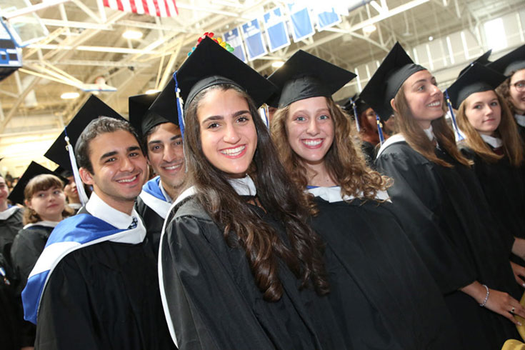 Group of undergraduates dressed in caps and gowns standing and smiling in Gosman.