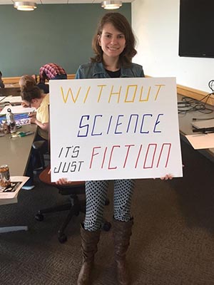Student holding her poster that says: Without Science it's Just Fiction 