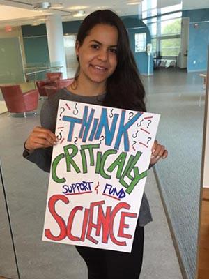 Student holding her poster which says: Think Critical -- Support & fund Science