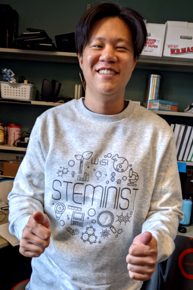 A member in a WiSI 'steminist' sweater smiles and gives a double thumbs up