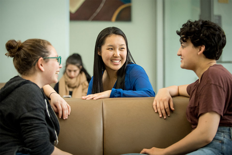 Three female students laugh and talk in a school lounge