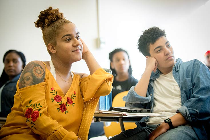 Two students seated in a lecture hall smiling at computers