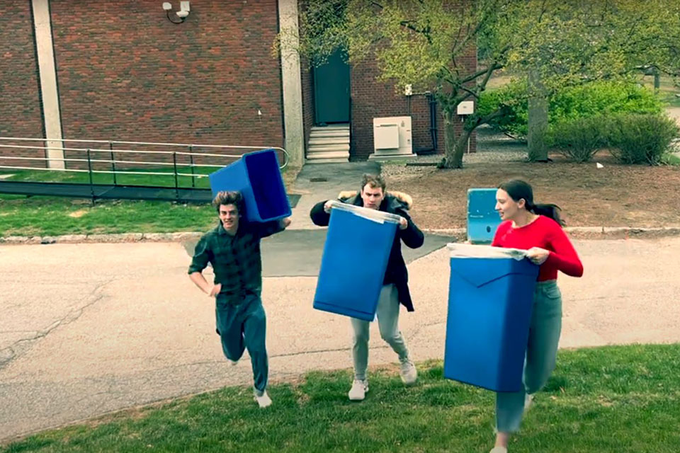 Three students holding recycling bins and running