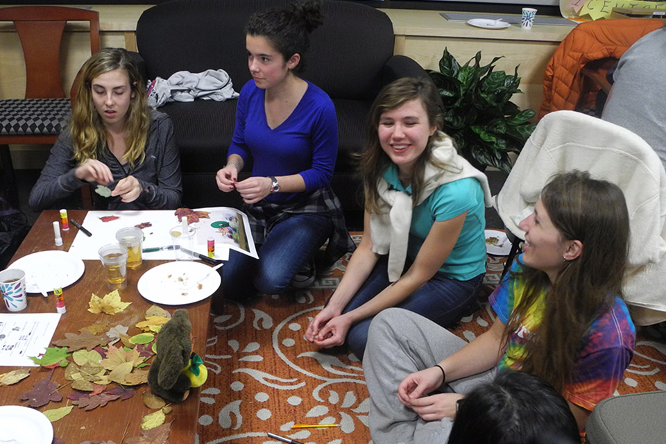 four female students seated around table, making crafts.