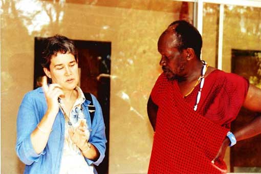 Dorothy Hodgson talking with man, standing side by side outside, in front of a neutral-colored building