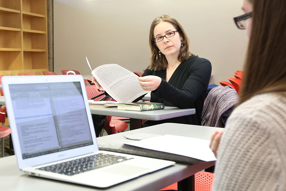 Professor Hannah Muller holding a paper and speaking with a student in class
