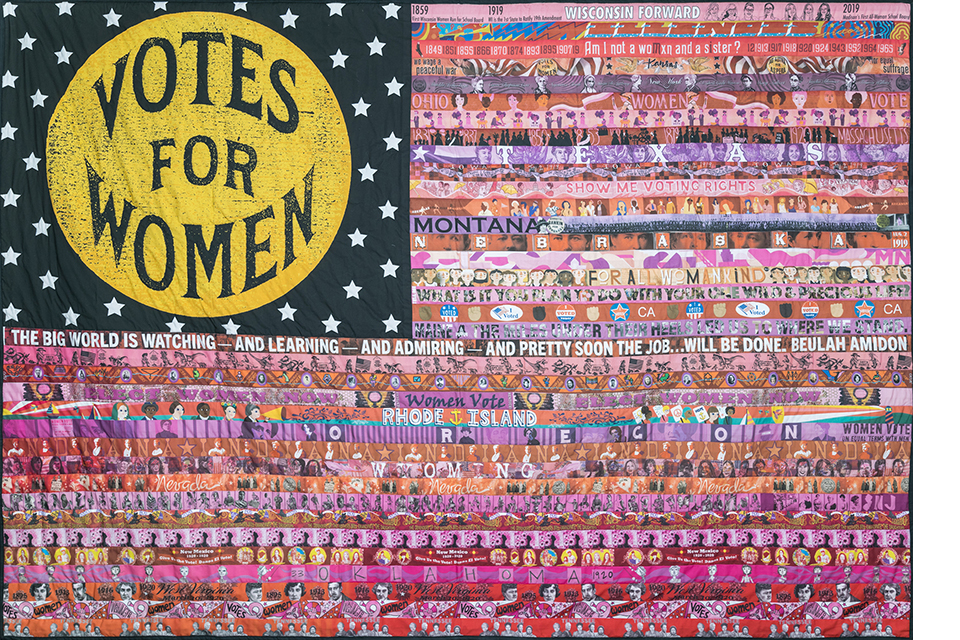 quilted flag by Marilyn Artus, has 36 colorful stripes representing 36 states that ratified the 19th amendment. the top left area says votes for women in black with gold letters