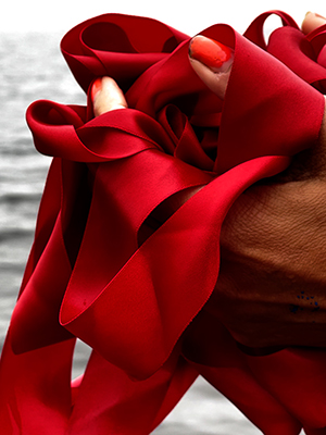 hands holding a bundle of red ribbon, a body of water can be seen in the background