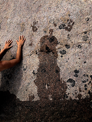 a rock wall with hands reaching in from the side, leaving wet hand prints