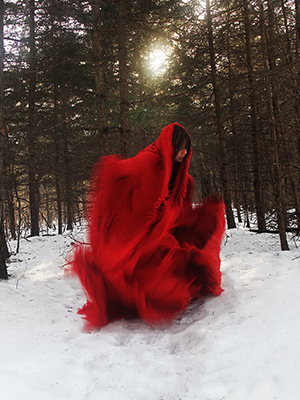 a woman wearing a red shawl dances in the snow covered forest. the garment is blurred with her movement
