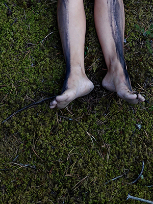 close up of feet, covered in charcoal, resting on mossy ground