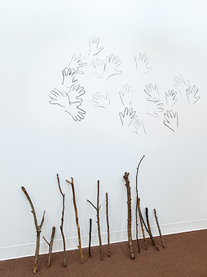 installation view Jaime Black exhibition, short sticks leaning on the wall, drawn handprints on the wall above the sticks
