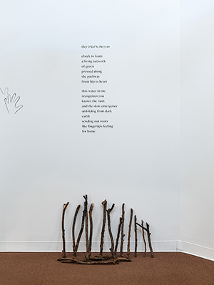 installation view Jaime Black exhibition, small sticks on the floor, leaned against the wall. a poem in black letters on the wall above the sticks