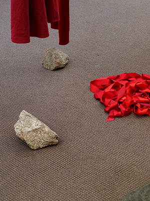 installation view Jaime Black exhibition, the bottom of red dresses, big rocks below, a pile of red ribbon in the center
