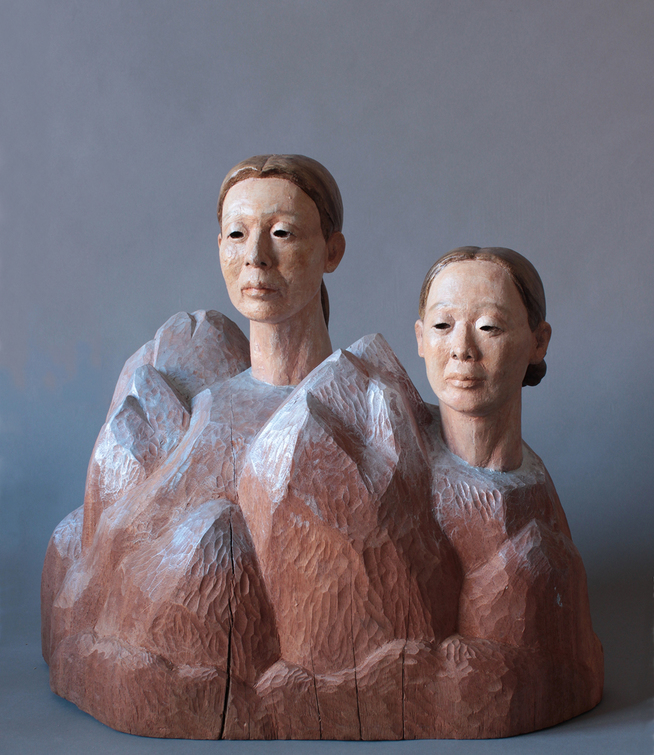 Sculpture by Sachiko Akiyama entitled "Where Earth Meets Sky, 2012. Wood, clay, paint. 19" x 13-1/2" x 17-1/2". Sculpture two elder Asian women's heads emerging from mountains.