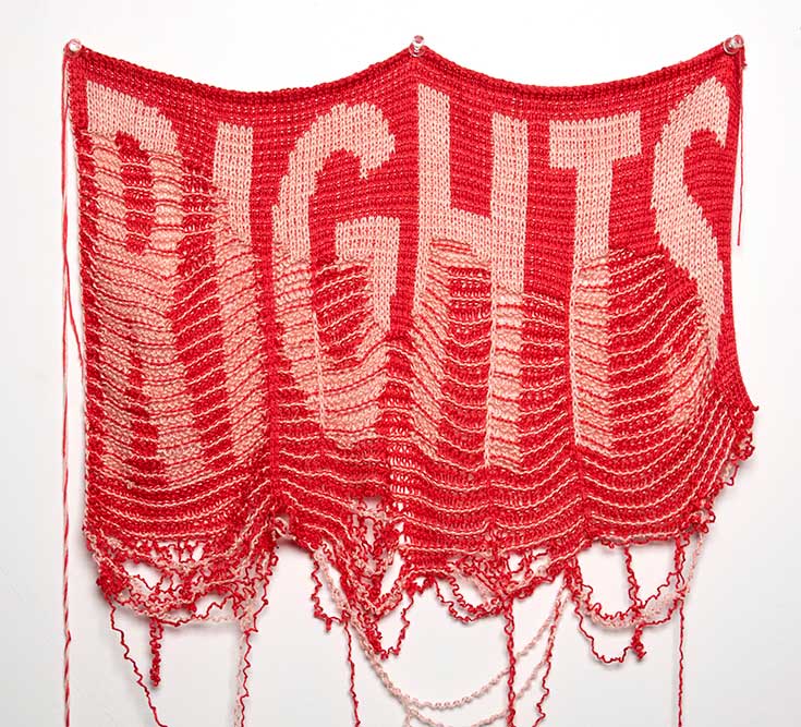 A video still of an unraveling red and pink textile piece displaying the word "RIGHTS"