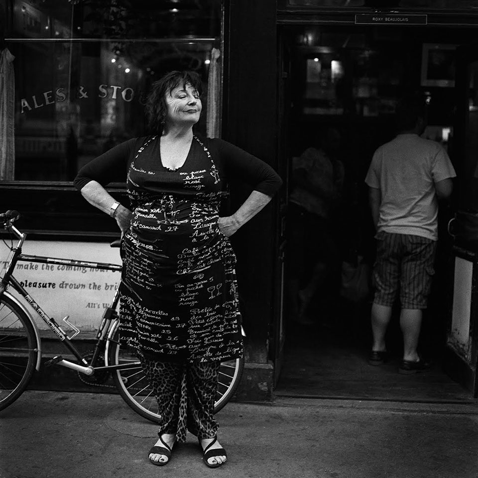 A woman stands in front of a shop with her hands on her hips