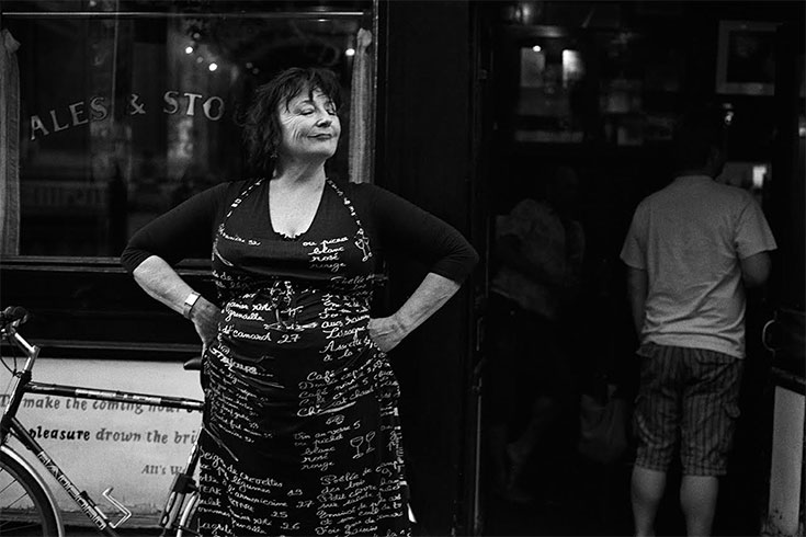 Black and white photograph of a woman standing outside of a store with her hands on her hips