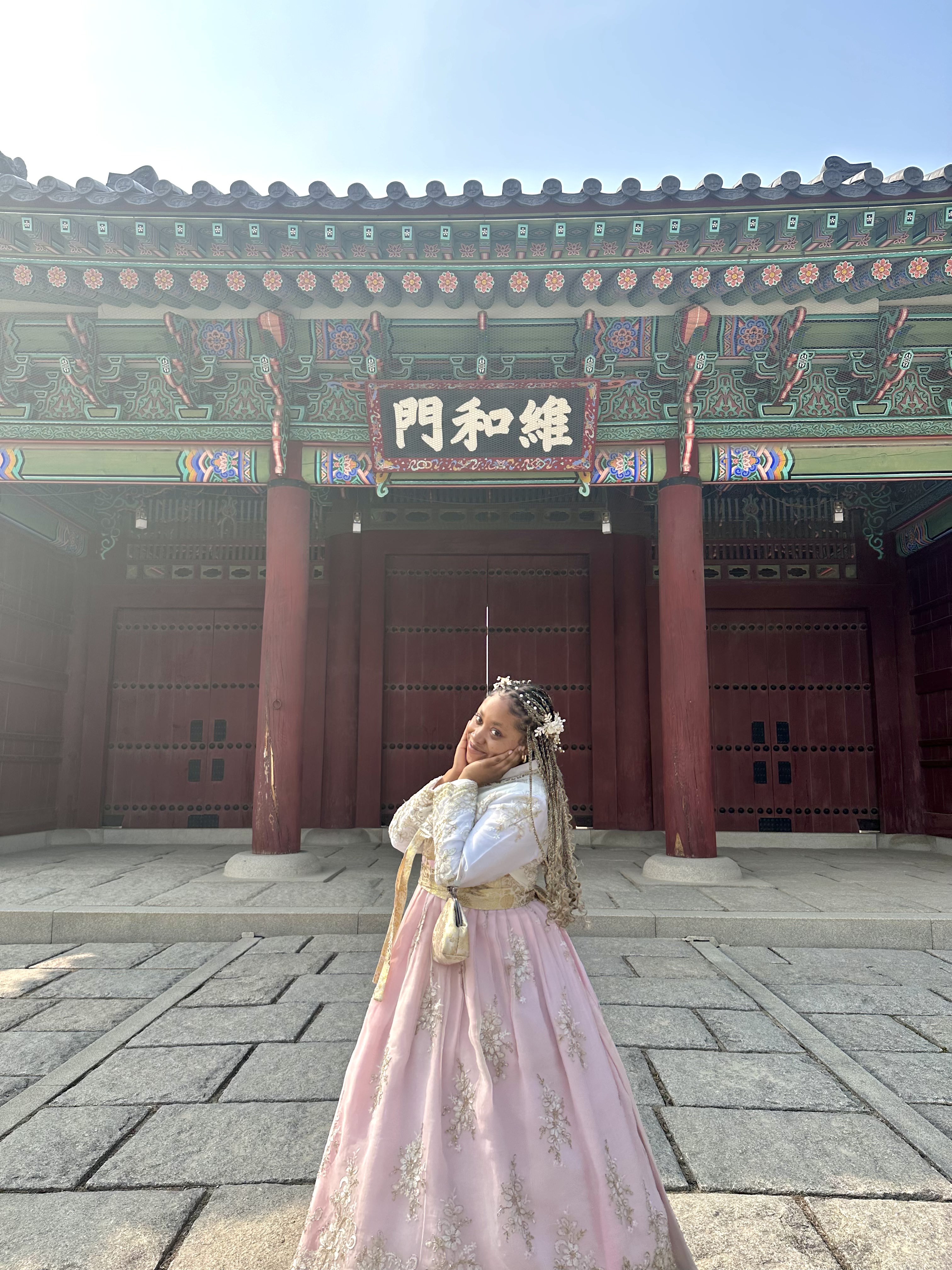 Floriesha standing in front of a Korean building in traditional clothing (a pink dress with gold detailing).
