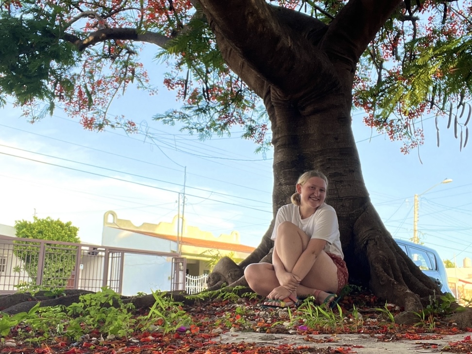 Cailan sits smiling underneath a tree on a sunny day in Mexico.