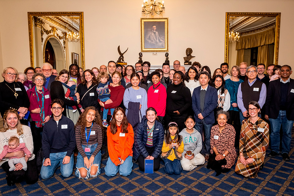 Approximately 50 people posing for a photo in front of two mirrors and a portrait in a fancy banquet hall.