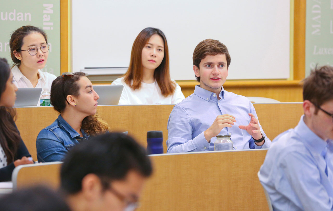 Young graduate students in a classroom. One student is making a comment to the professor. 